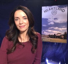 a woman is standing in front of a sign that says heartland on the side