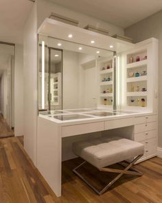 a dressing room with a stool and lighted mirror on the wall, along with shelving units