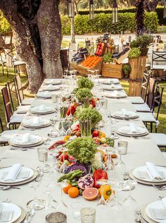 a long table is set with plates, silverware and fruit for an outdoor dinner