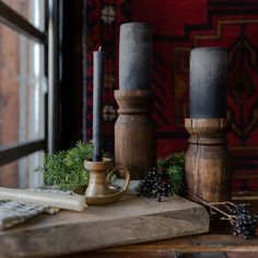 two candles are sitting on a cutting board next to some grapes and other items in front of a window