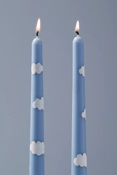 two blue candles with white clouds on them are shown in front of a gray background