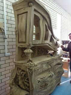 a man standing in front of a large wooden cabinet with carvings on the doors and drawers