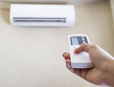 a person holding a remote control in front of an air conditioner