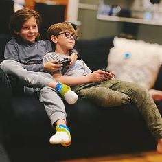 two young boys sitting on a couch playing video games with remote controllers in their hands