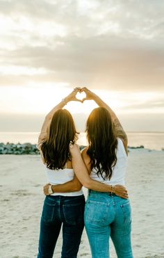 two women standing on the beach making a heart shape with their hands while holding each other's hands