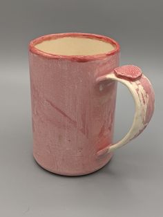 a pink coffee mug with a white handle on a gray surface, in the shape of a heart