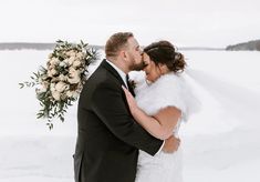 a bride and groom standing in the snow kissing each other with their arms around each other