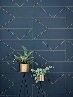 two metal planters with plants in them against a blue tiled wall, one is gold and the other has white flowers