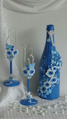 two wine glasses, one with blue flowers and the other decorated with white pearls are sitting next to a bottle