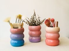 three different colored vases with brushes in them on a white counter top next to each other