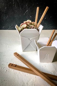 two white containers with chopsticks in them next to each other on a table