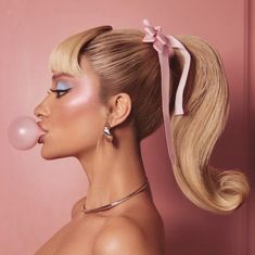 a woman with blonde hair blowing bubbles on her nose and wearing a pink bow around her neck