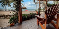 a wooden chair sitting on top of a wooden deck next to the ocean and palm trees