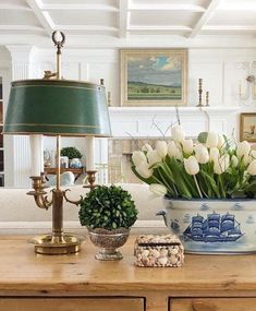 a table topped with a vase filled with white tulips and a green lamp