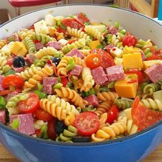 a large bowl filled with pasta salad on top of a wooden table