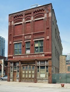 an old red brick building sitting on the corner of a street in front of tall buildings