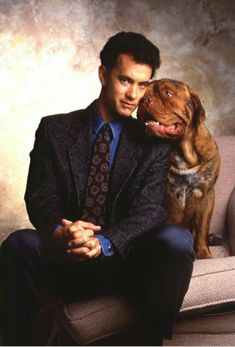 a man in a suit and tie sitting on a couch next to a brown dog