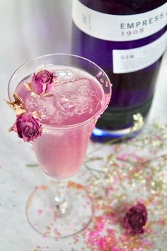 a glass filled with pink liquid and flowers next to a bottle of wine on a table