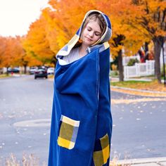 a woman in a blue and yellow blanket is standing on the sidewalk with her hands behind her head