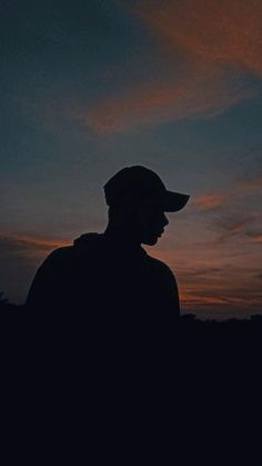 the silhouette of a man wearing a hat in front of an orange and blue sky