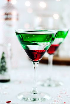 two martini glasses with red and green liquid in them sitting on a table next to confetti