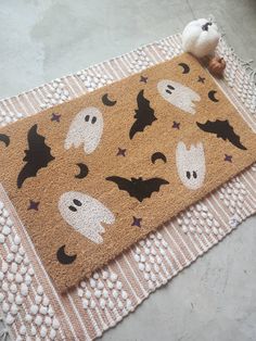 a halloween door mat with bats and ghost faces on it next to a stuffed animal