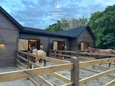 two horses are standing in front of a barn with wooden fences and doors on each side