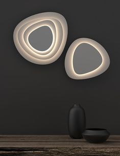 two circular lights on the wall next to a vase and black object in front of it