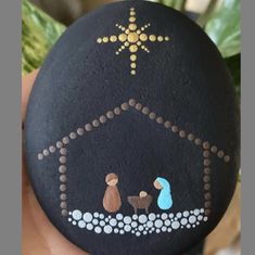 a hand holding a rock with a nativity scene painted on it's side