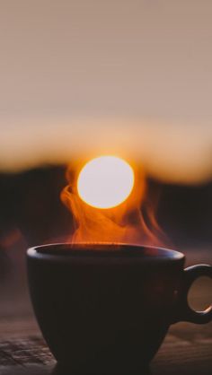 a coffee cup sitting on top of a wooden table with the sun setting in the background