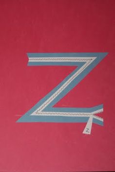 the letter z is made up of strips of blue tape and some white thread on a pink background