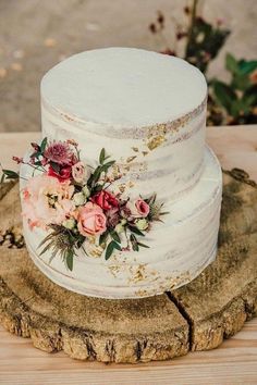 a white wedding cake with flowers on the top is sitting on a piece of wood