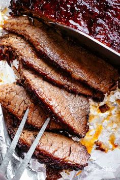 sliced meat on tin foil with tongs and barbecue sauce in the backgroud