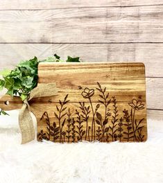 a wooden cutting board with flowers on it and a ribbon tied around the edge, sitting on a white furnishing