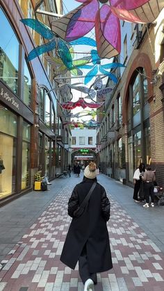 a person walking down a street with umbrellas hanging from the ceiling