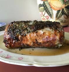 a piece of meat covered in sauce on a white plate next to a flower pot