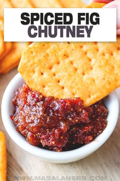 a hand holding a cracker over a bowl filled with chili sauce and cheese chips