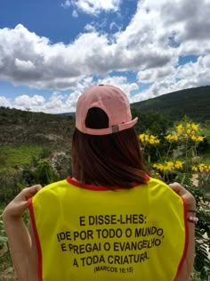 a woman wearing a yellow vest and pink hat standing in front of wildflowers