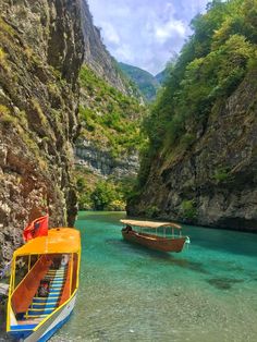 two boats floating on top of a river next to a cliff