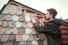 a man standing next to a building with lots of tiles on it's side