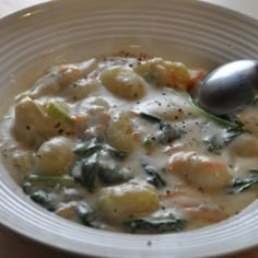 a white bowl filled with soup on top of a wooden table next to a silver spoon