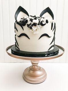 a white cake with black and white frosting on a metal stand in front of a white wall