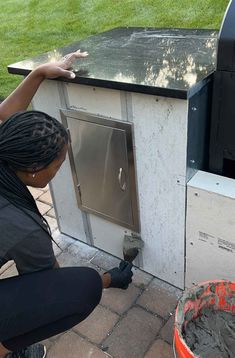 a woman kneeling down next to a grill