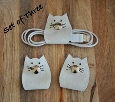 three white leather cats plugged into a charger on a wooden surface with the words set of three written above them