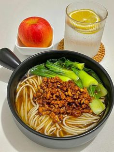 a bowl filled with noodles and vegetables next to an apple