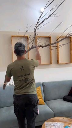 a man is standing in front of a couch with branches hanging from it's ceiling