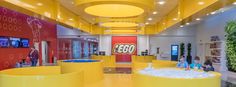 the inside of a lego store with yellow and red walls, people sitting in chairs