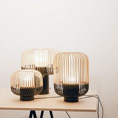 three lamps sitting on top of a wooden table next to a white wall and floor