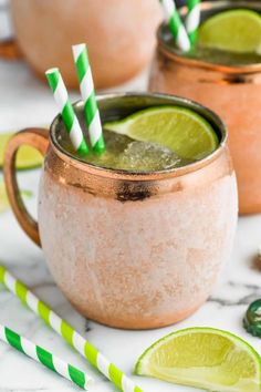 two glasses filled with green and white drink next to lime slices on a marble table