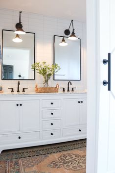 a white bathroom with double sinks and mirrors on the wall next to an open door